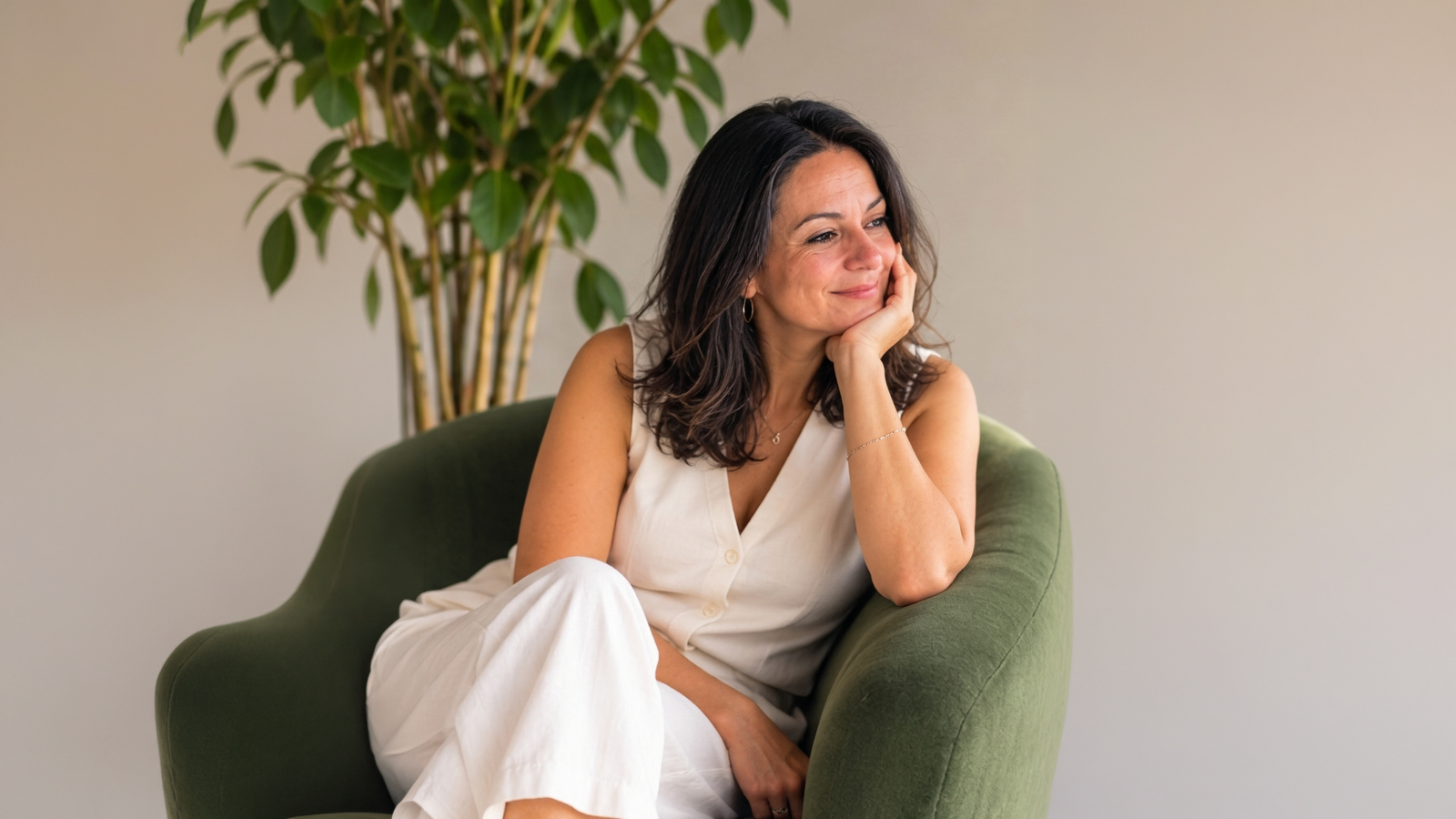Susana de la Cruz sentada en un sillón verde junto a una planta, con la mano en la mejilla y la mirada fuera de cuadro